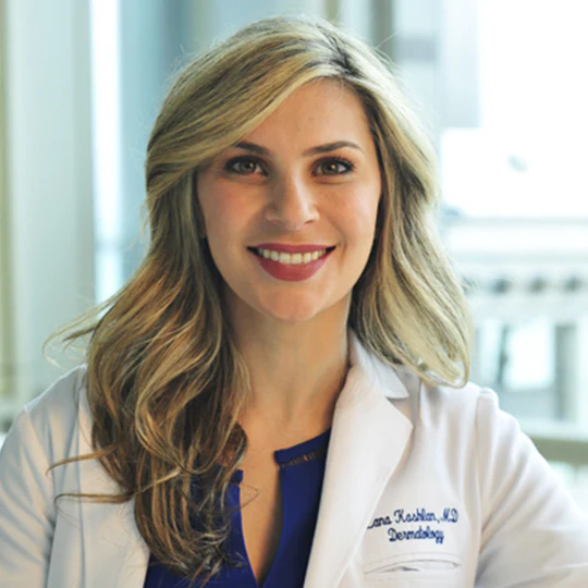 A smiling woman in a white lab coat stands indoors, with 